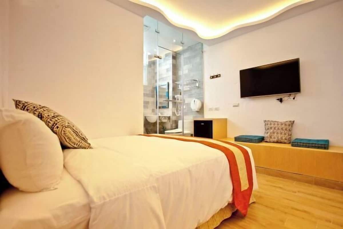 A modern hotel room with a bed, a TV mounted on the wall, and a glass shower enclosure.