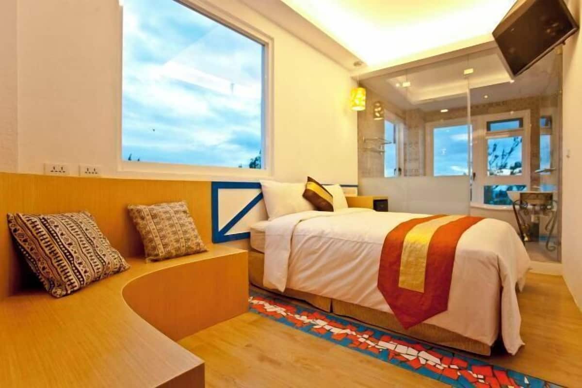 A modern hotel room with a large bed, a curved seating area, a large window, and a TV mounted on the wall.
