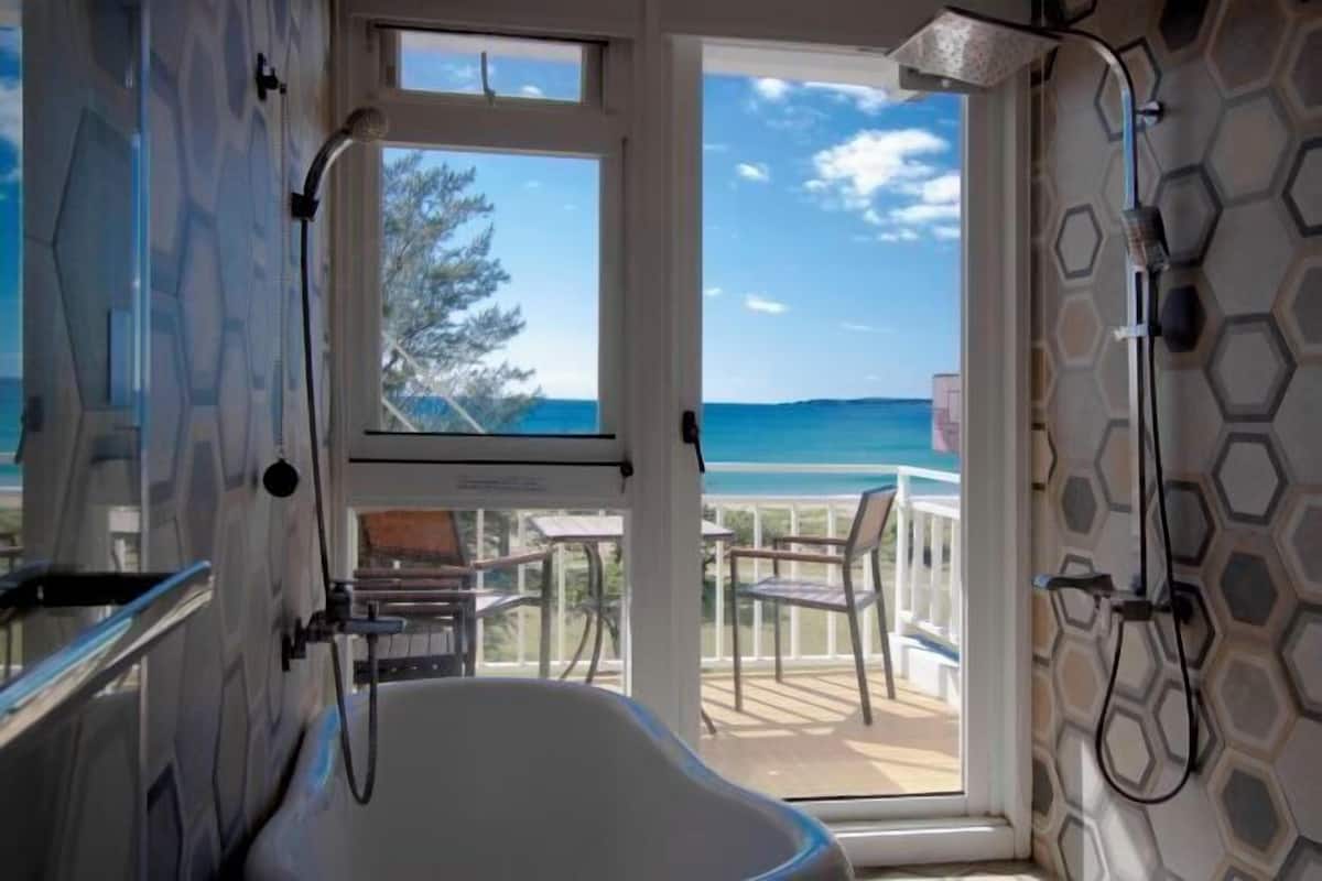 A bathroom with a bathtub, a shower, and a view of the ocean through a large window.