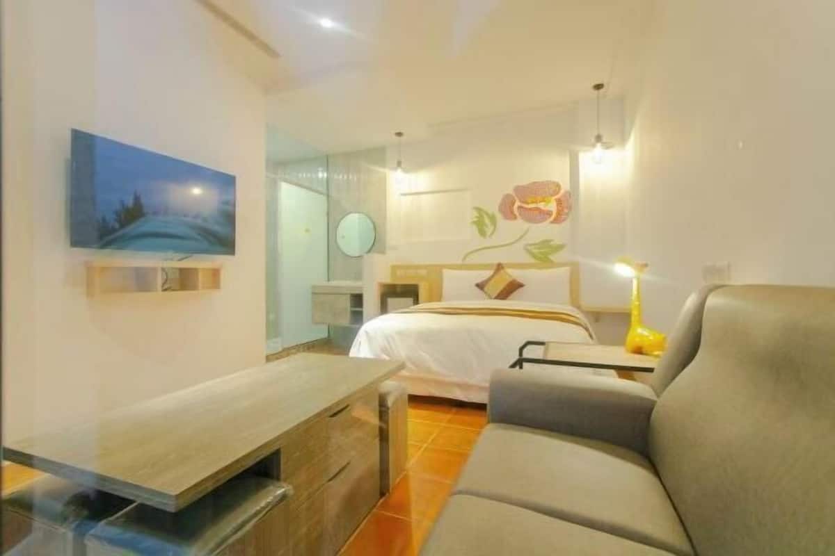 A modern hotel room with a bed, a sofa, a desk, and a painting on the wall.