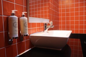 Une salle de bain avec un lavabo blanc, deux distributeurs de savon liquide et un miroir au-dessus du lavabo.