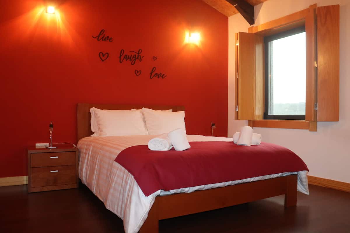 A bedroom with a red wall, a bed with white bedding, and a window with curtains.