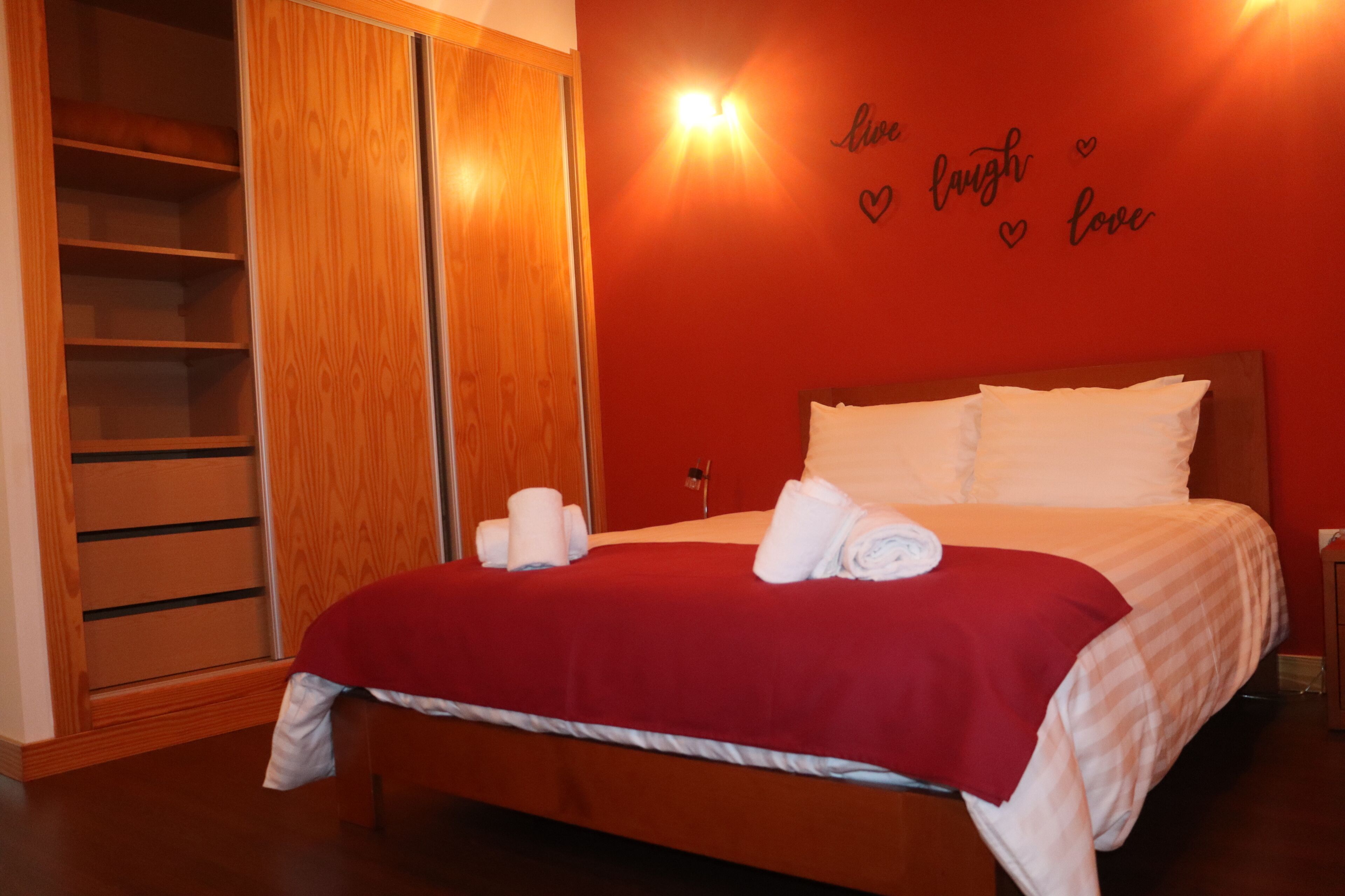 Ett hotellrum med en garderob i trä, en säng med vita sängkläder och en röd vägg med en hjärtformad dekoration.