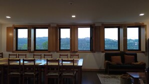 Un salon spacieux avec un coin repas, de grandes fenêtres offrant une vue sur un paysage vallonné et un canapé confortable.