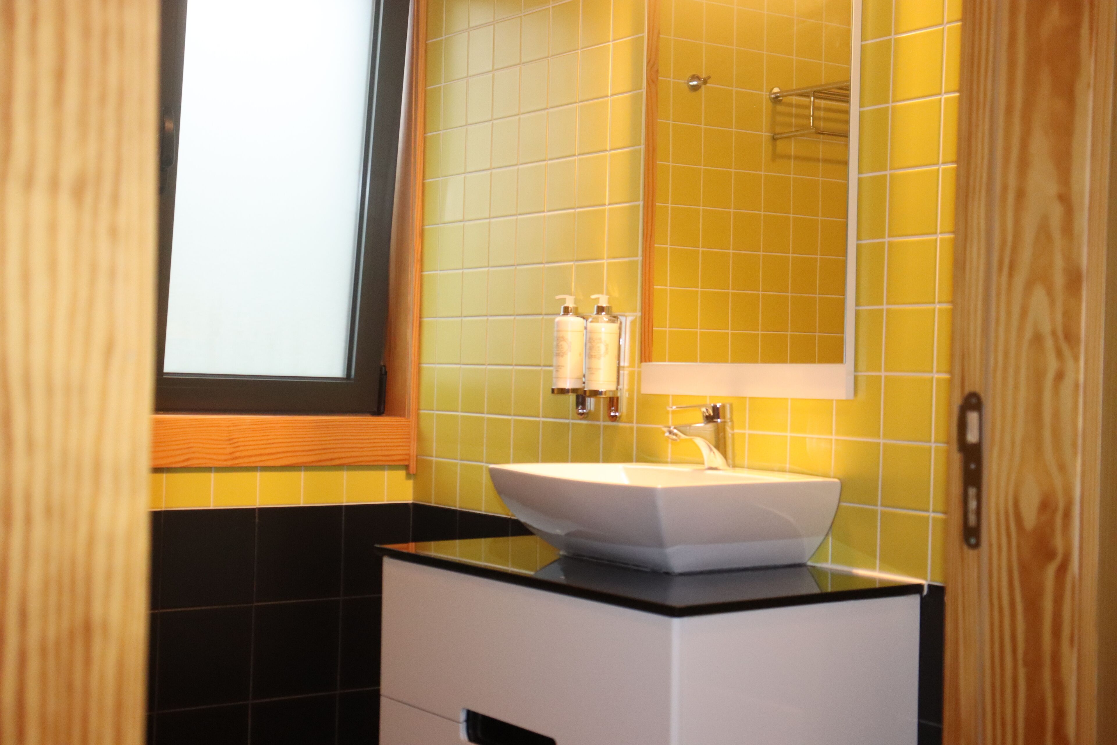 A bathroom with a white sink, a mirror, and yellow-tiled walls.