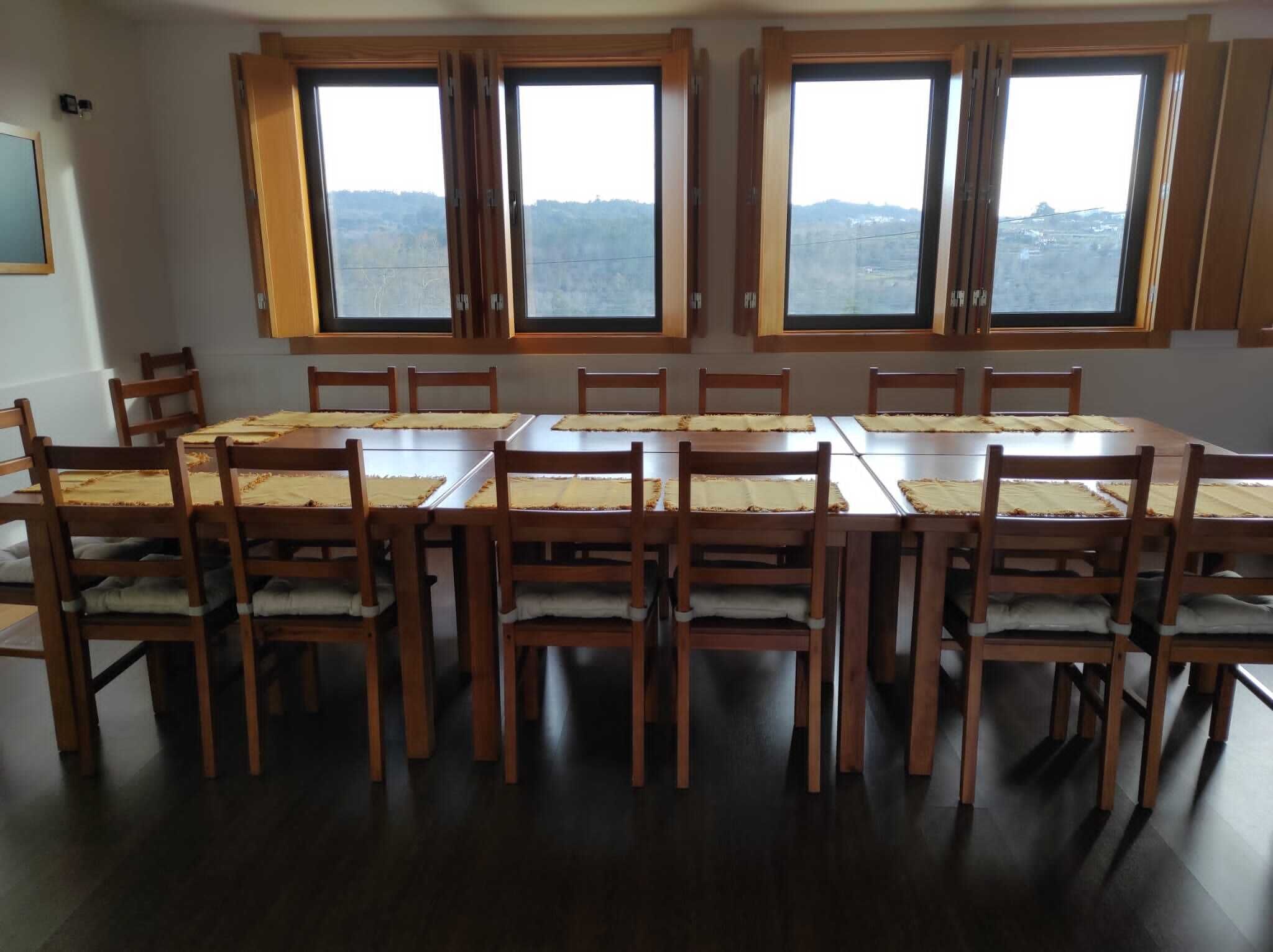 Uma sala de jantar com uma grande mesa de madeira e cadeiras, janelas amplas com vista para uma paisagem montanhosa.
