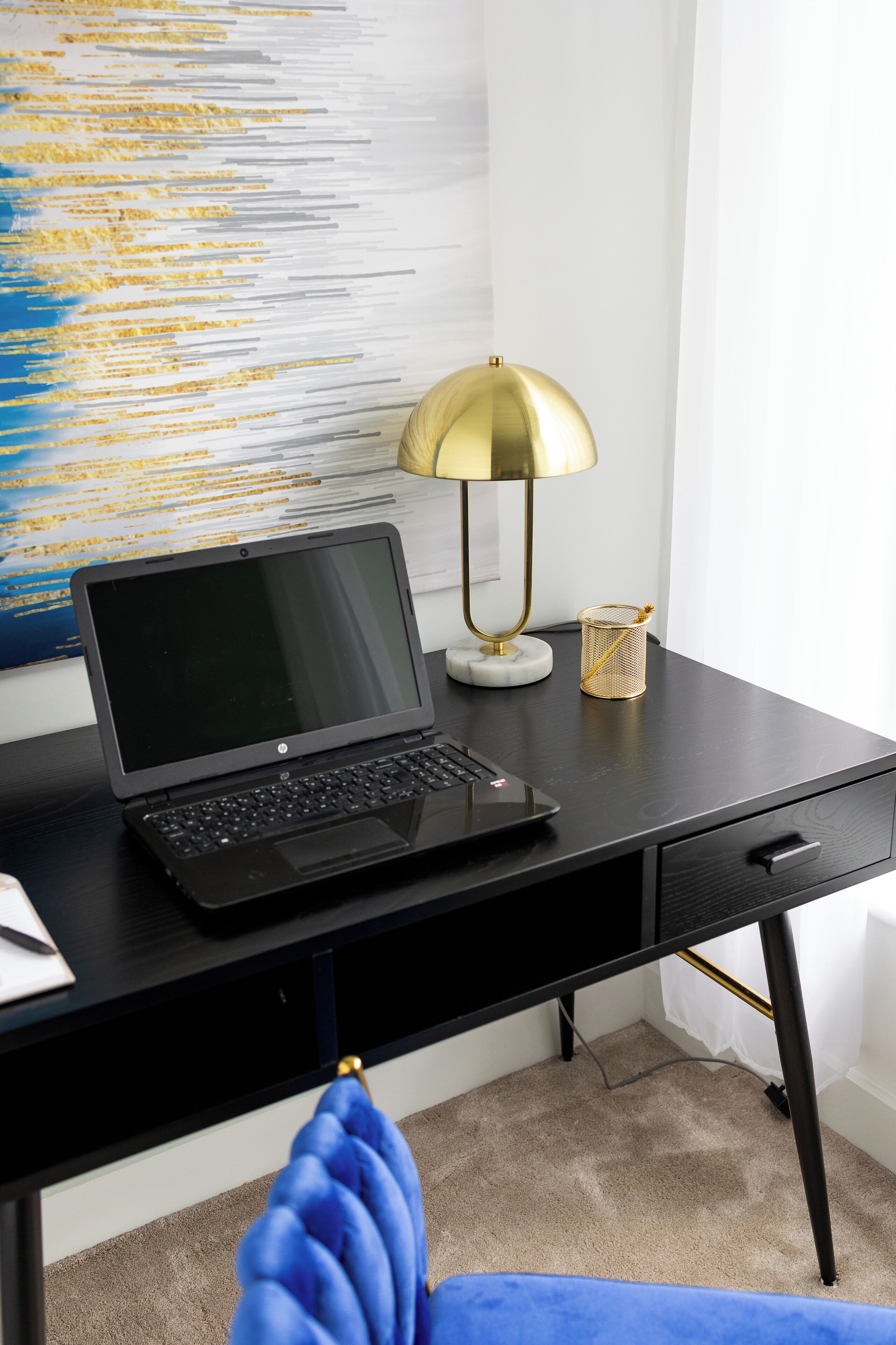 A black desk with a laptop, a gold lamp, and a small decorative item.
