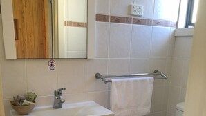 Un baño con un lavabo blanco, un espejo, un mueble con puertas de vidrio, un perchero y un inodoro.