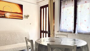 A room with a round table, a sofa, a door, and a window with curtains. - RM08 - Senigallia, two-room apartment facing the sea (Senigallia)