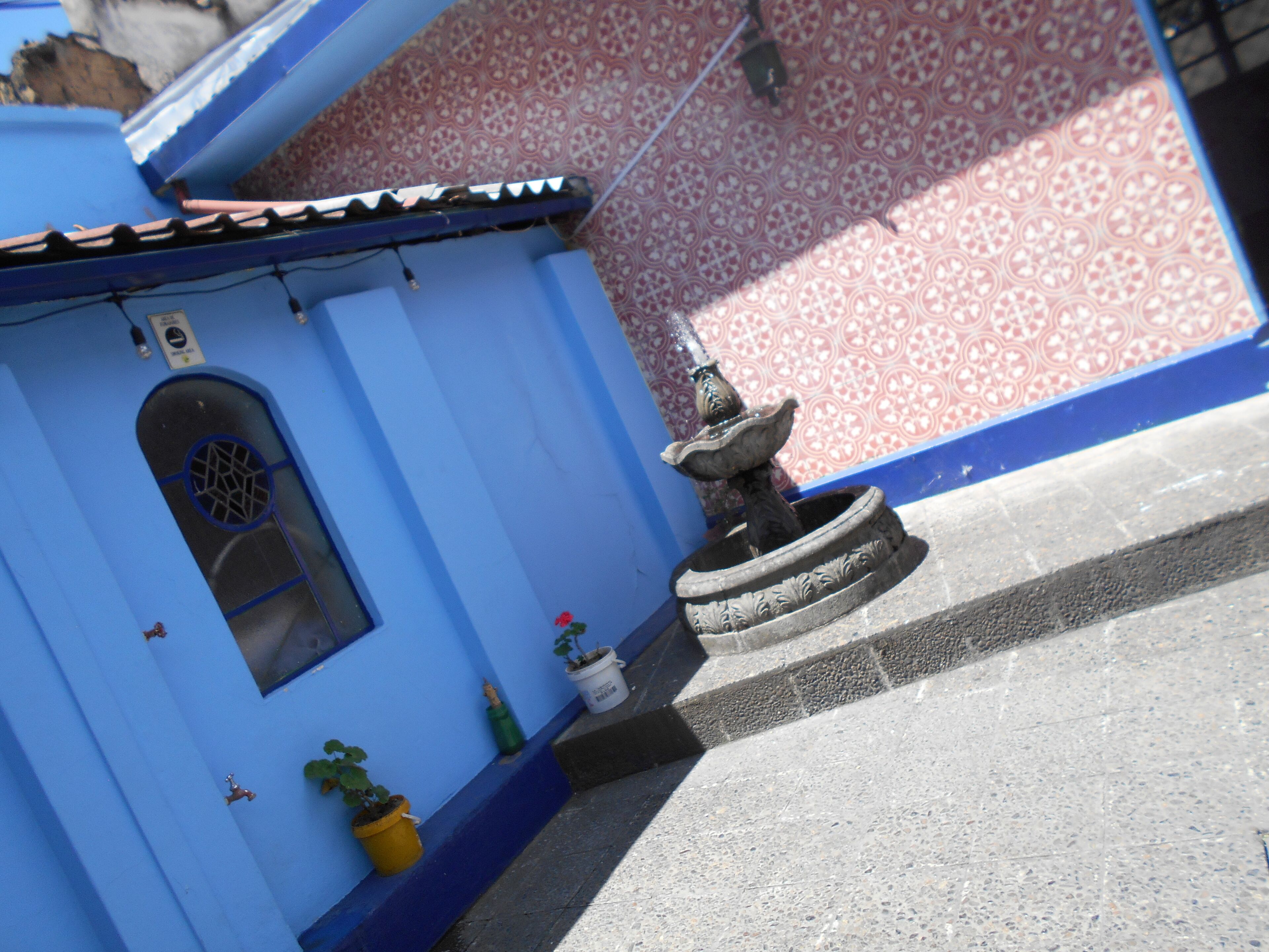 A building with a blue facade, a small window with a decorative grille, and a stone fountain.