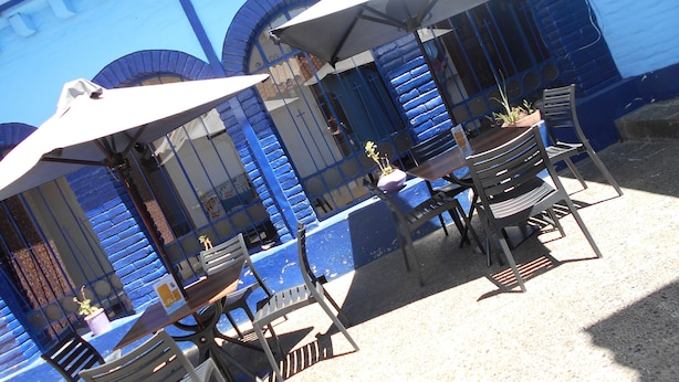 Buiten zitplaatsen met parasols, een blauw gebouw met bogen en een kleine tafel met een plant.