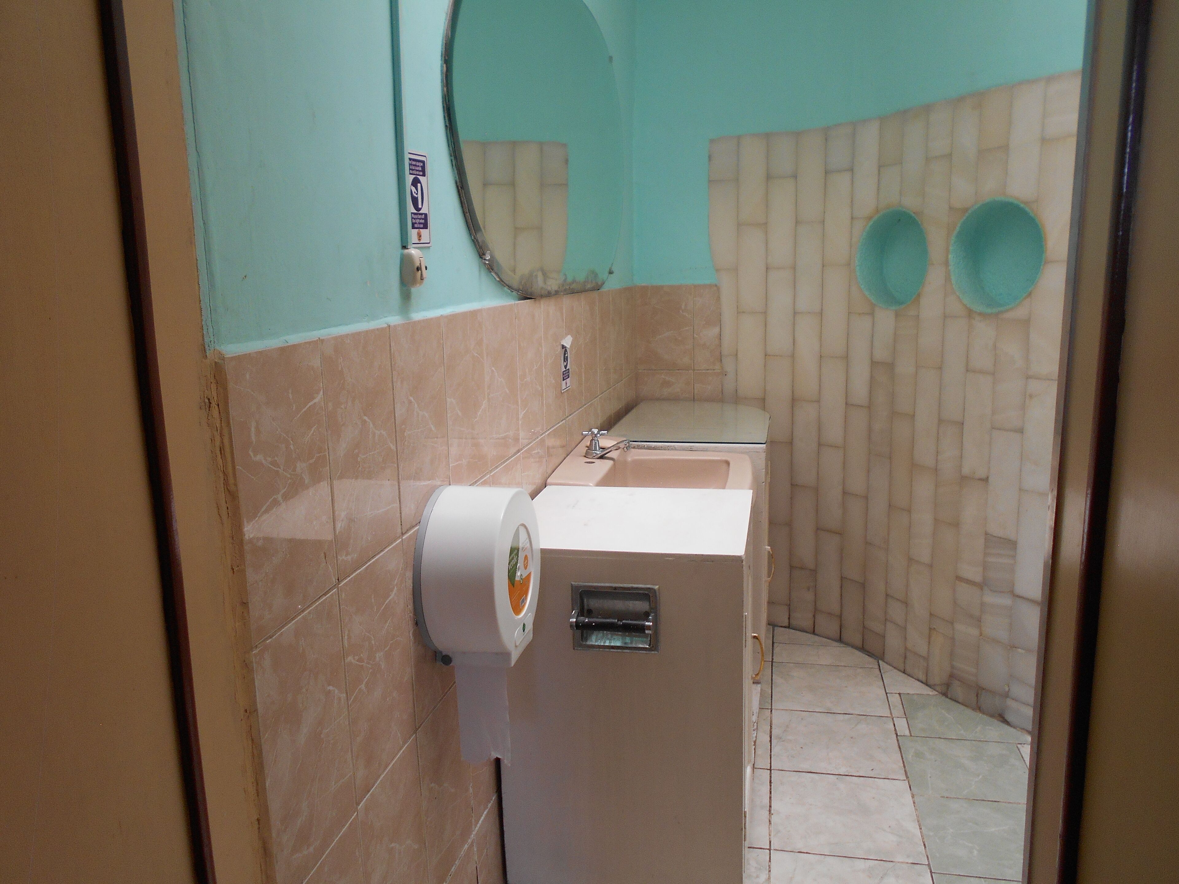 Un baño con inodoro, lavamanos y dos pequeños espejos redondos.