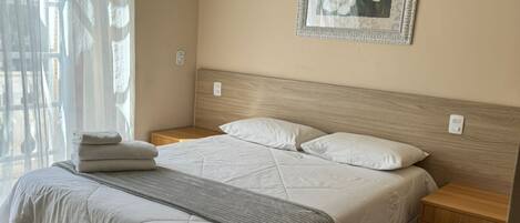 A neatly made bed with a headboard, a bedside table with a drawer, and a framed picture on the wall.