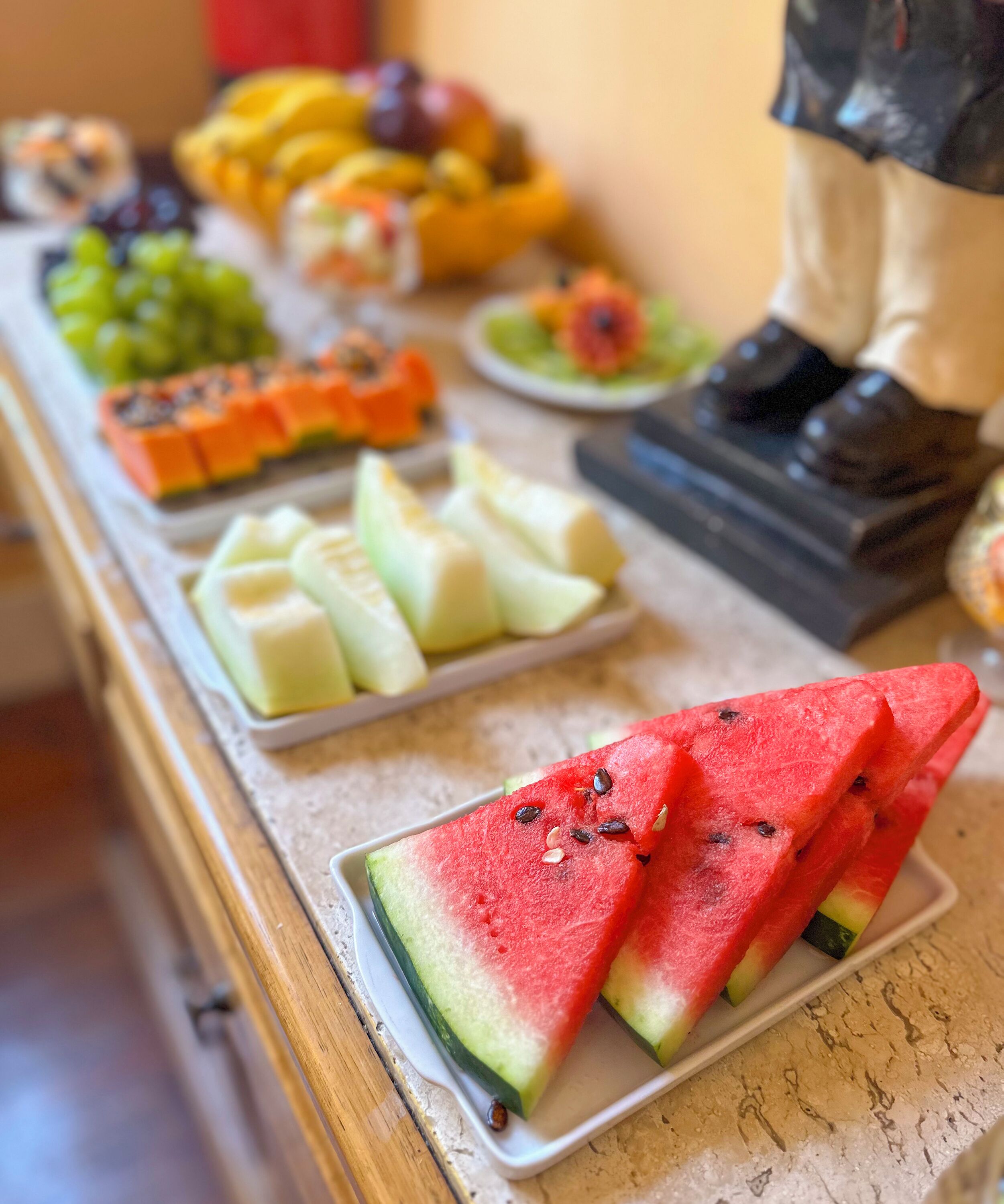 Une table de buffet garnie de divers fruits et ornée d’une statue.