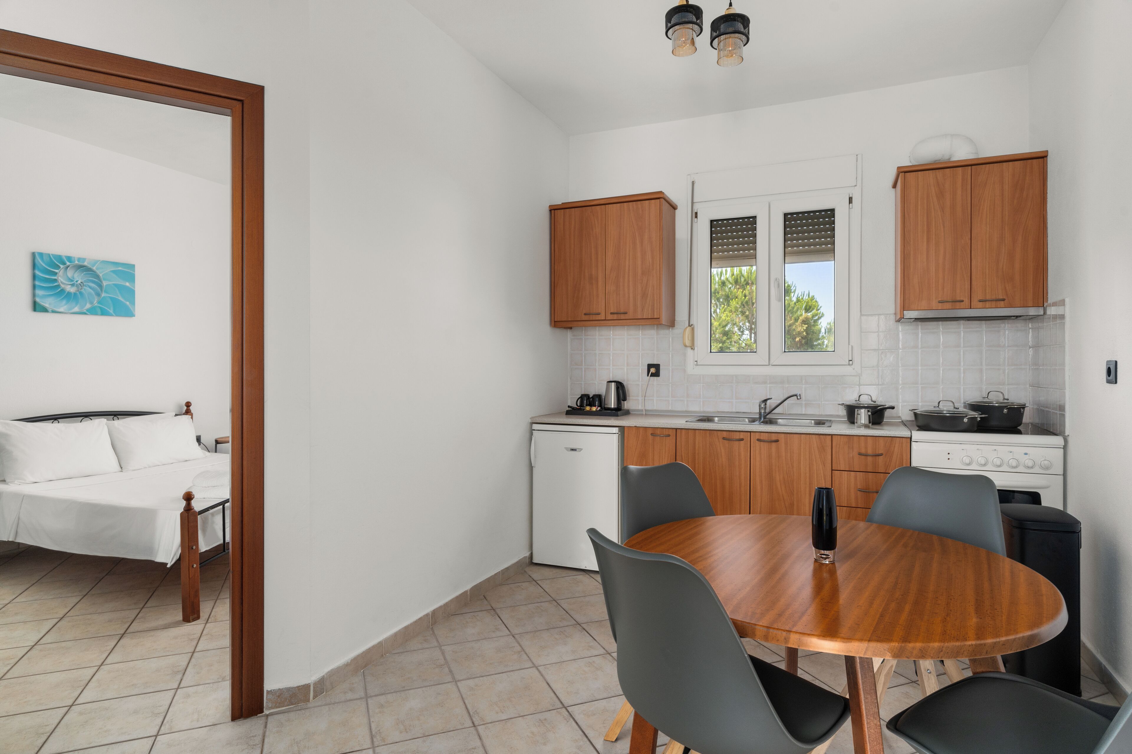 Una cucina funzionale con mobili in legno, un tavolo da pranzo con sedie, un piccolo frigorifero e una finestra con persiane.