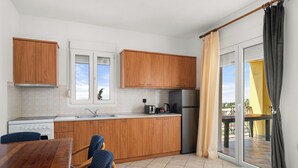 A modern kitchen with wooden cabinets, a stainless steel refrigerator, and a dining area with a glass table and chairs. - The Dandy Horizon (Igoumenitsa)