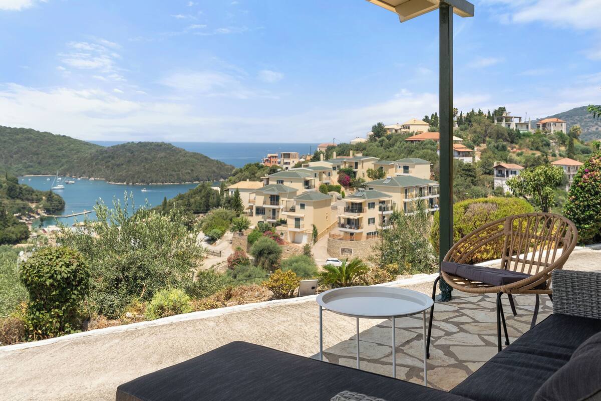 A terrace with a view of a coastal town, a wicker chair, and a small table.