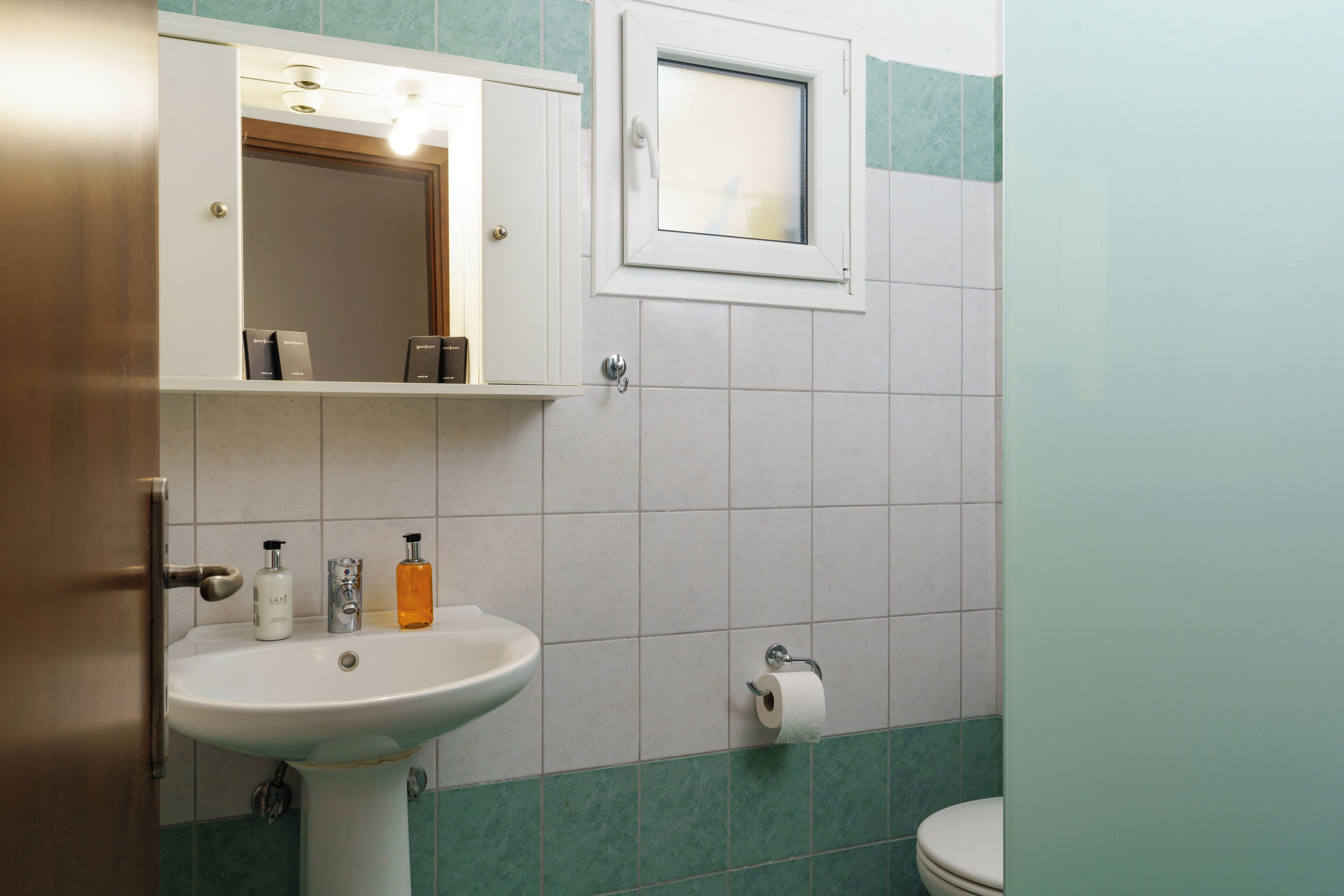A bathroom with a white sink, a mirror, a window, and a toilet.