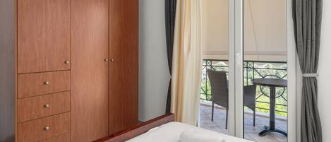 Un dormitorio con un armario de madera, una cama con ropa de cama blanca y un balcón con mesa y sillas.