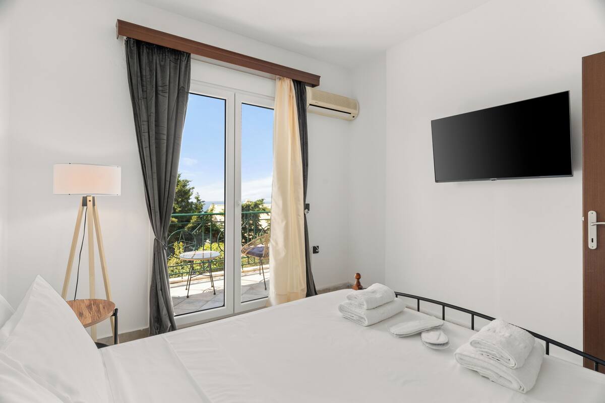 A hotel room with a bed, a flat-screen TV, a window with curtains, and a view of the outdoors.