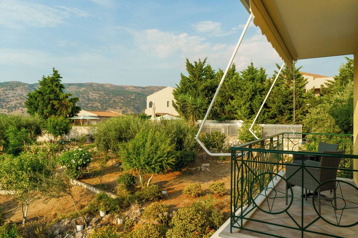 A balcony with a view of a garden and distant hills.