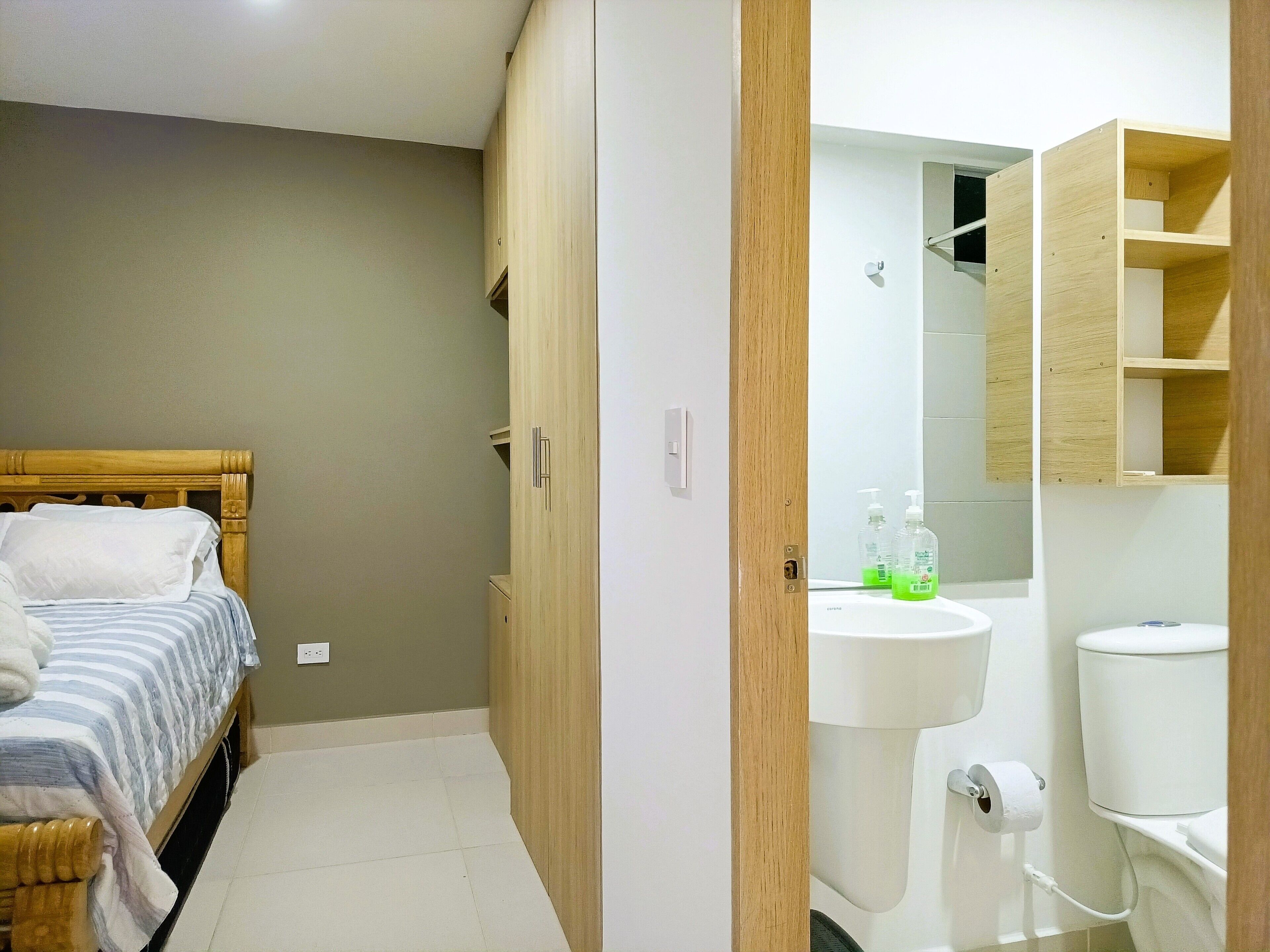 Un dormitorio con cama, armario de madera y baño con inodoro, lavamanos y espejo.
