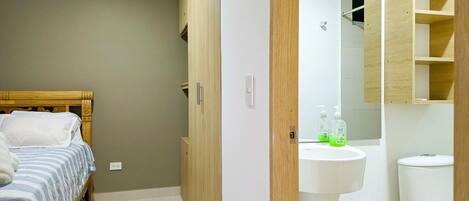 Un dormitorio con cama, armario de madera y baño con inodoro, lavamanos y espejo.