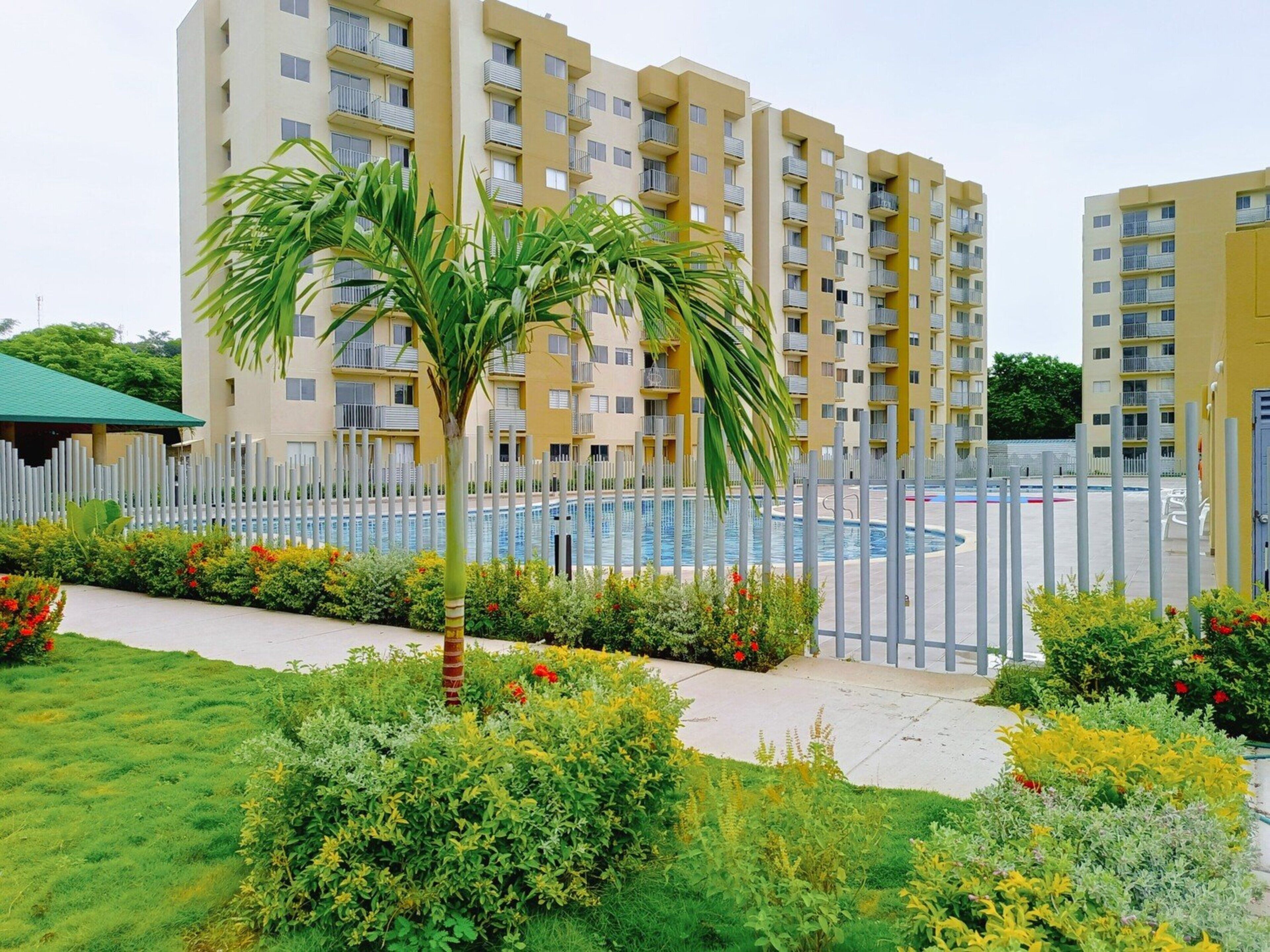 A residential building with multiple balconies, a swimming pool, and a well-maintained garden with various plants and flowers.