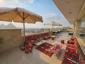 An outdoor terrace with seating, tables, and umbrellas, overlooking a cityscape and distant pyramids. - Pyramids Tower Inn (Giza)