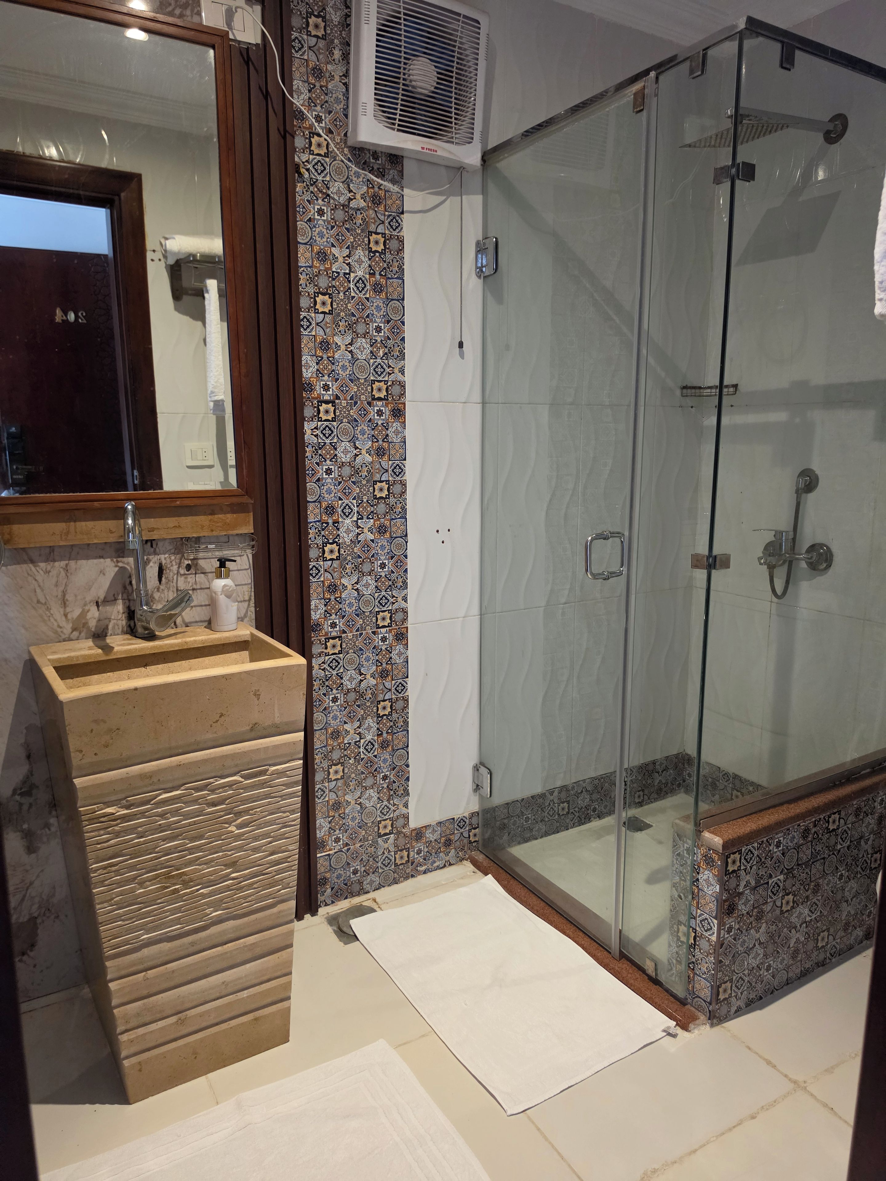 Un baño con ducha envuelta en vidrio, lavamanos con encimera de mármol y espejo sobre el lavamanos.