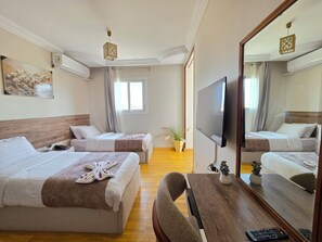 Ein Hotelzimmer mit zwei Betten, einem Fernseher, einem Holztisch und einem großen Spiegel.