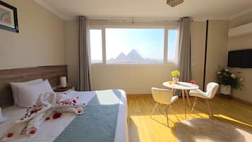 Habitación de hotel con cama, escritorio, silla, televisor y vista a las pirámides.