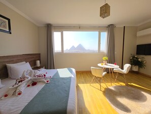 Ein Hotelzimmer mit Bett, Schreibtisch, Sessel, Fernseher und Blick auf Pyramiden.
