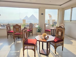 A balcony with a view of pyramids, wooden chairs with red cushions, and a table with a vase of flowers. - Pyramids Tower Inn (Giza)