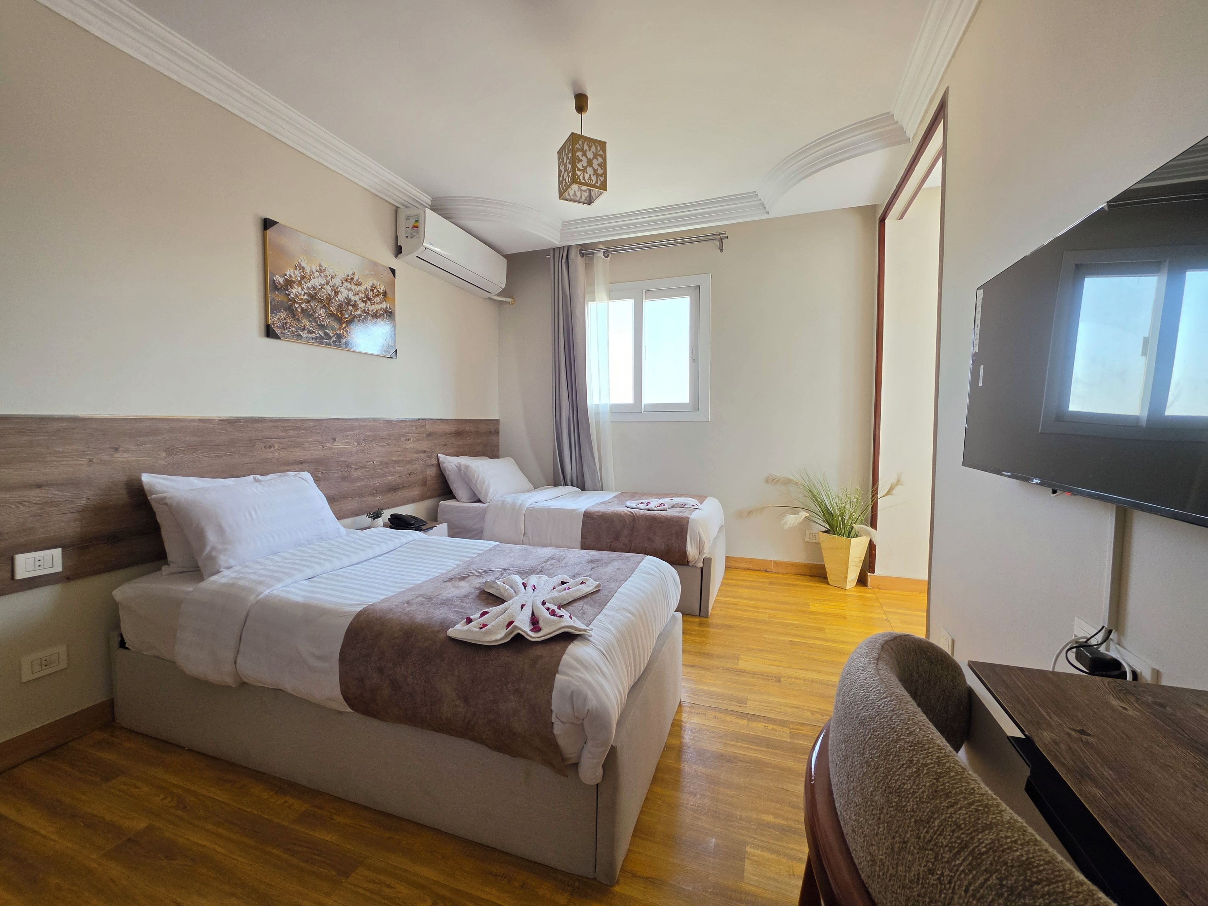 Habitación de hotel con dos camas, una televisión de pantalla plana, suelo de madera y una lámpara en el techo.
