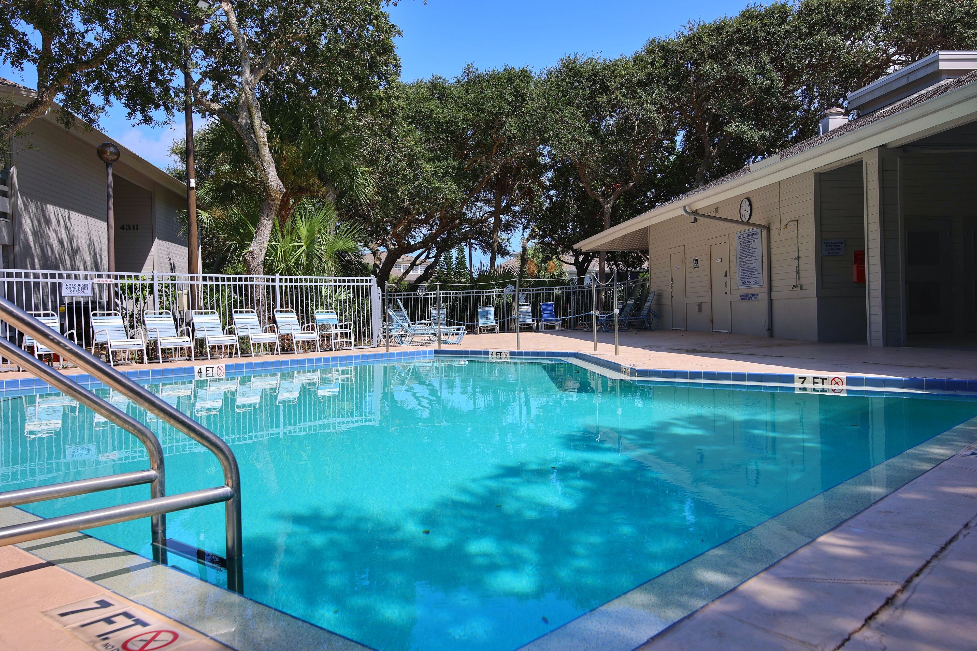 A swimming pool with a metal railing, lounge chairs, and a covered area with a clock.
