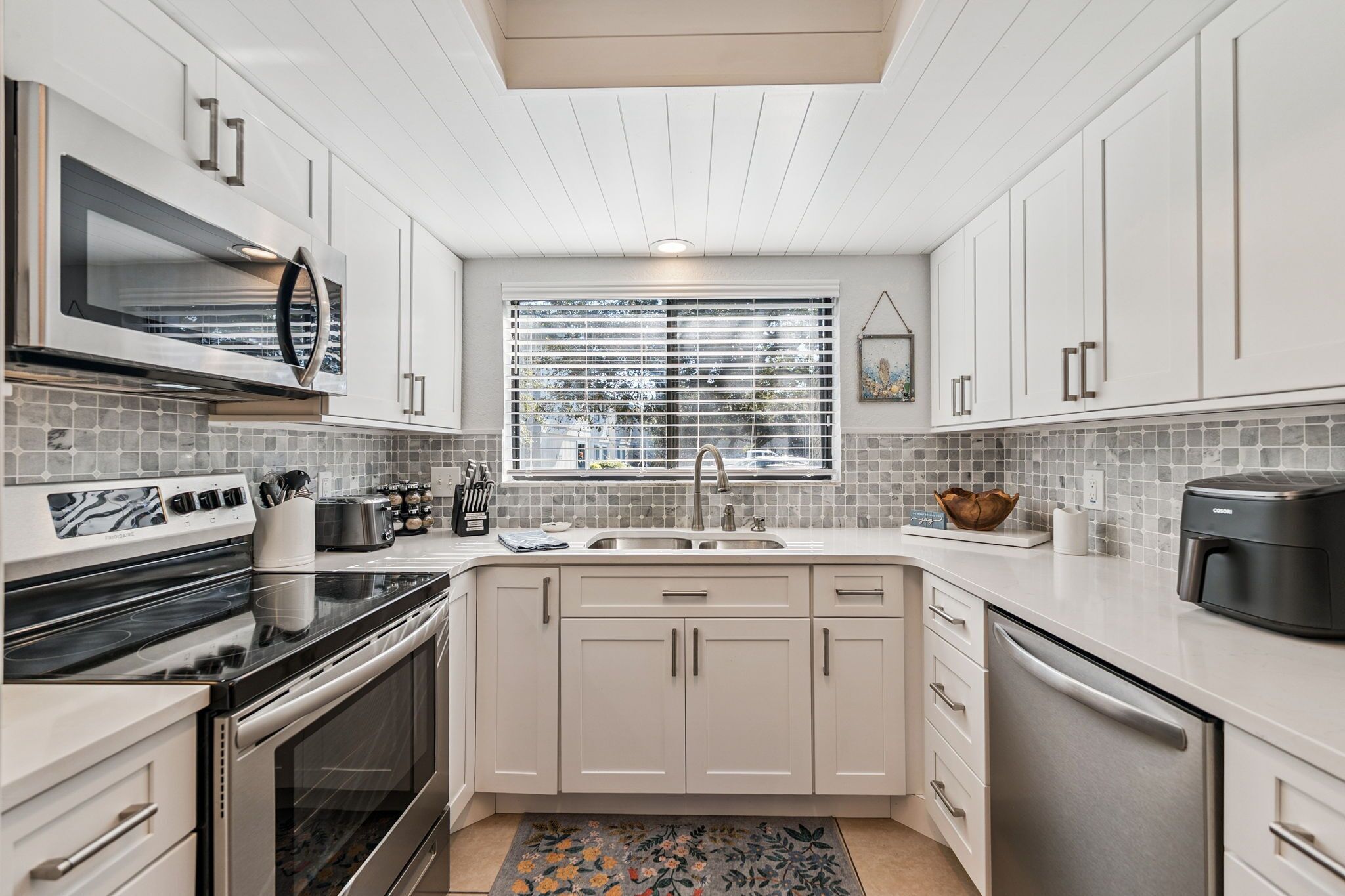 A modern kitchen with white cabinetry, a built-in oven, a microwave, a sink, and a coffee maker.