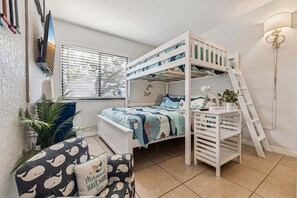 A bunk bed with a desk and ladder, a window with blinds, and a chair with a whale pattern pillow.