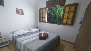 Camera da letto con un letto, un comodino, una finestra con vista sul verde e un quadro appeso al muro.