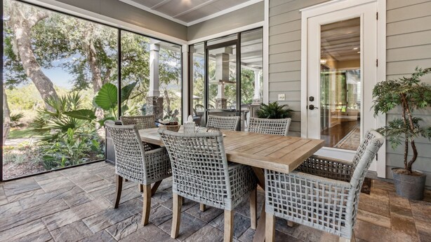 Un espace de restauration en plein air avec des chaises en osier et une table en bois, de grandes fenêtres et une vue sur les arbres et les plantes.