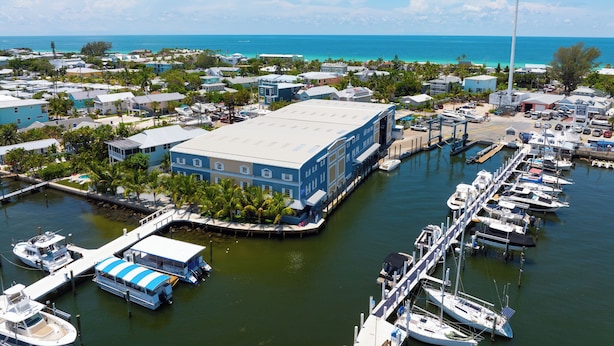 A marina with multiple boats docked, a large building with a blue roof, and a clear view of the ocean. - AMI Condo W/ Heated Pool, Walk to Beach & Bridge St (Bradenton Beach)
