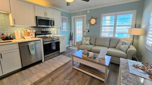 A modern kitchen with white cabinets, a microwave, and an oven. There's a beige sofa and a coffee table in the living area. - AMI Condo W/ Heated Pool, Walk to Beach & Bridge St (Bradenton Beach)