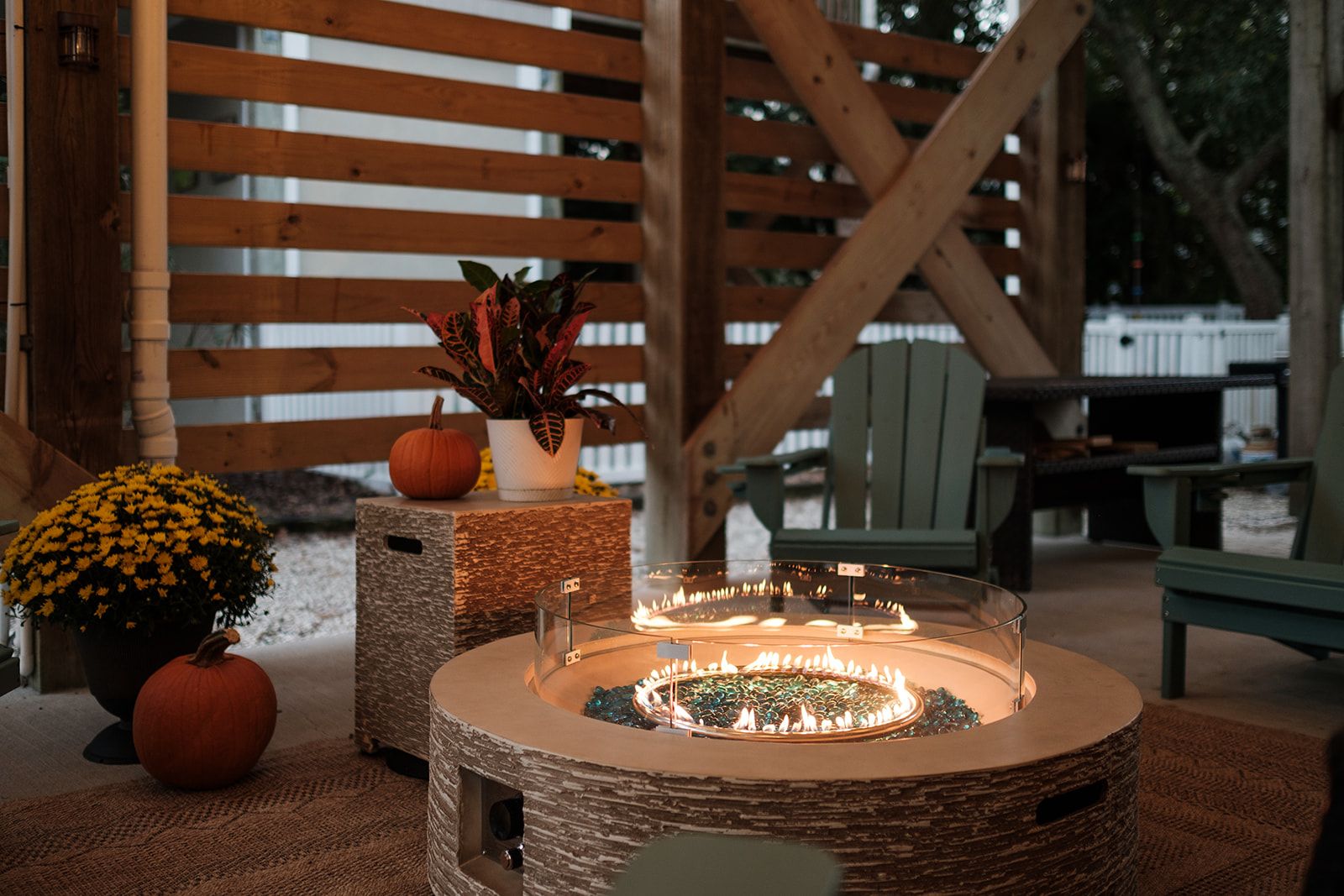 A round outdoor fire feature with a glass enclosure, surrounded by rustic wooden furniture and decorative elements.