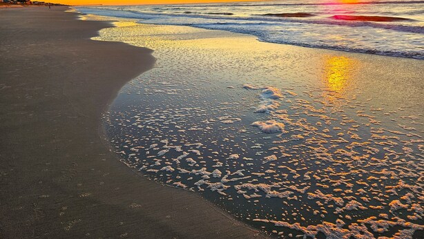 Une plage au coucher du soleil, où les vagues viennent doucement lécher le rivage.