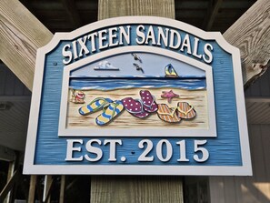 A sign for Sixteen Sandals with a beach scene, including flip-flops and a starfish, established in 2015. - Private Beach Access |Sound Views |Elevator (Surf City)