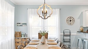 Une salle à manger avec une longue table, des sets de table, un lustre et un vase rempli de fleurs.