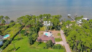 An aerial view of a property with a swimming pool, a large house, and a dock extending into a body of water.