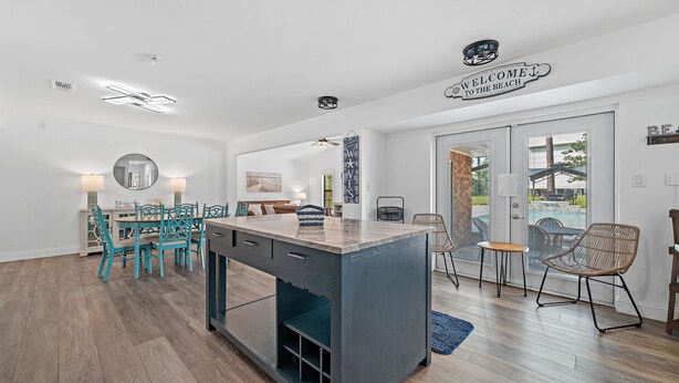 A modern kitchen with a central island, a dining area with teal chairs, and a sign reading "WELCOME TO THE BEACH".