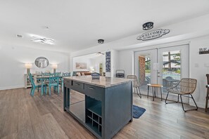 Une cuisine moderne avec un îlot central, un coin repas avec des chaises de couleur turquoise et un panneau indiquant : « BIENVENUE À LA PLAGE ».