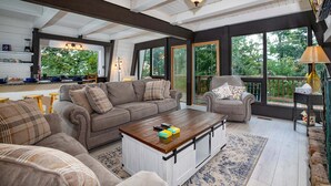A spacious living area with a large sofa, a coffee table, and a view of the outdoors through large windows. - Country Squire Cabin - private 180 degree mountain views! (Basye)